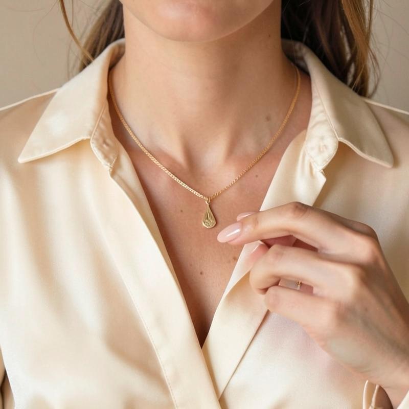 Main avec manucure nude ajustant un collier doré
